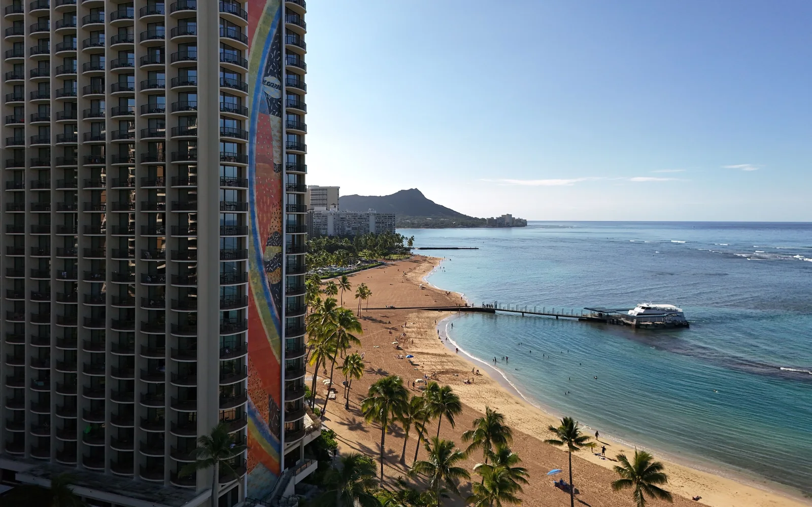 An aerial view of Hilton Hawaiian Village's Rainbow Tower beside Waikiki Beach, with Diamond Head in the distance
